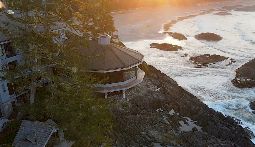 <p>A scenic view of The Pointe Restaurant nestled among trees and perched on rugged shoreline. The ocean waves are gently crashing against the rocks, and the sun is rising, casting a warm glow over the landscape.</p>