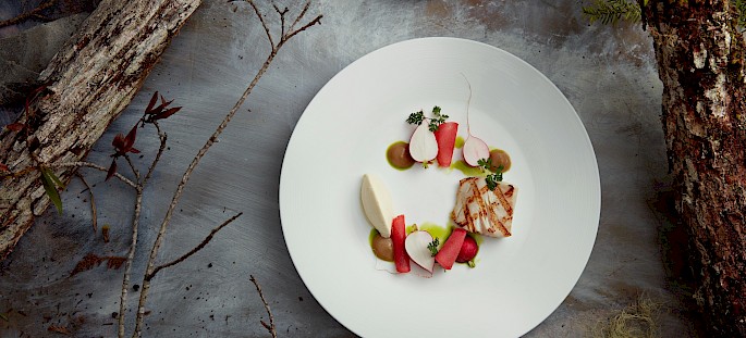 Dish of sablefish and seasonal vegetables set on a forest floor background
